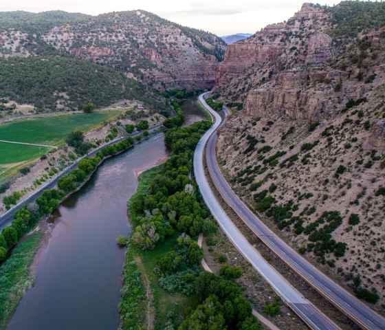 Photo of road stretching into the distance in between a cliff face and river